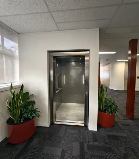 Stainless steel passenger lift in an office building with planters either side, installed by Lift Ease