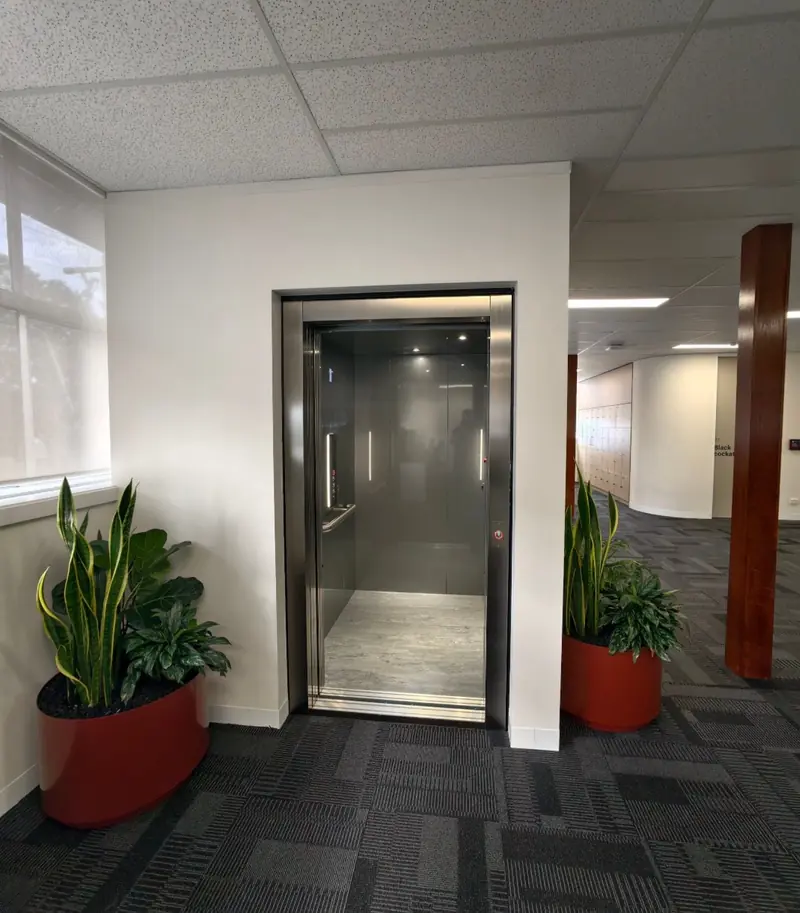 Stainless steel passenger lift in an office building with planters either side, installed by Lift Ease