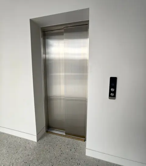Stainless steel commercial lift doors with a landing call panel, installed by Lift Ease