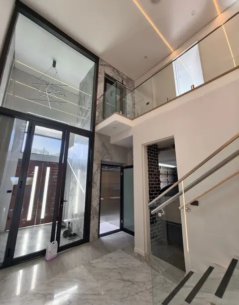 Home lift with black glass doors in a double-height marble foyer, installed by Lift Ease