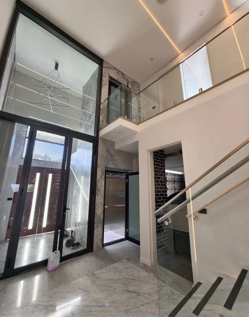 Home lift with black glass doors in a double-height marble foyer, installed by Lift Ease