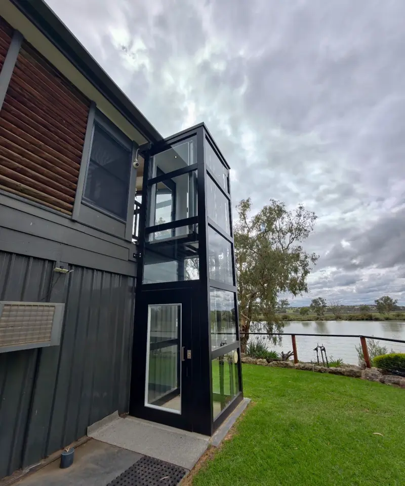 External glass lift shaft on a two-storey home beside a river, installed by Lift Ease