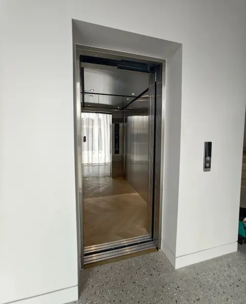 Stainless steel lift with doors open onto a herringbone timber floor, installed by Lift Ease