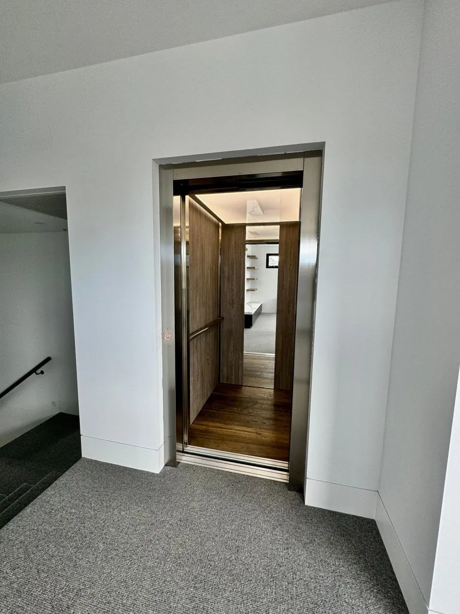 Completed modern elevator with dark wood interior doors and stainless steel frame in bright commercial space